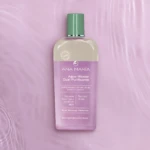 Botella de Agua Micelar Dual Ana María con arroz morado y lavanda, sobre fondo rosa con textura ondulada.