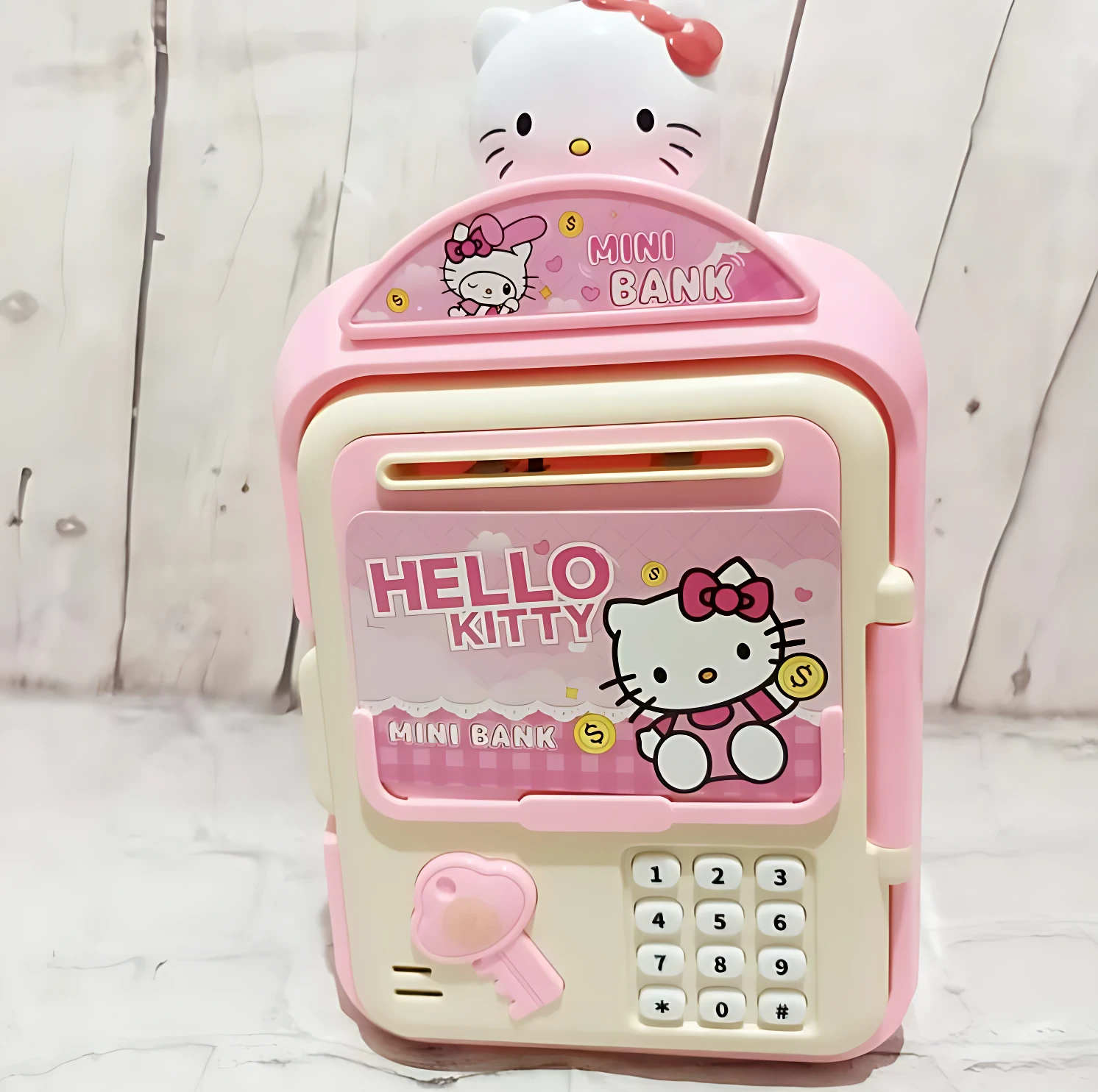 Alcancía tipo cajero electrónico en rosa con diseño de Hello Kitty, incluye teclado numérico, ranura para monedas y llave decorativa.