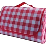 Alfombra de picnic enrollada con diseño a cuadros rojos y blancos, incluye asa roja para transporte.