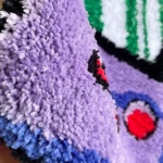 Alfombra de teléfono gamer retro en poliéster, vista de primer plano mostrando textura de pelusa suave en tonos morado, azul y detalles rojos y negros.