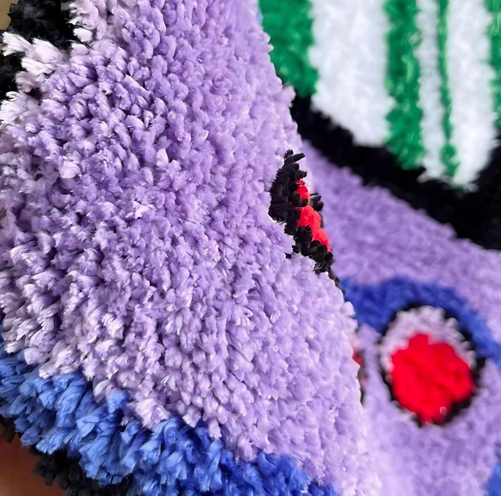 Alfombra de teléfono gamer retro en poliéster, vista de primer plano mostrando textura de pelusa suave en tonos morado, azul y detalles rojos y negros.