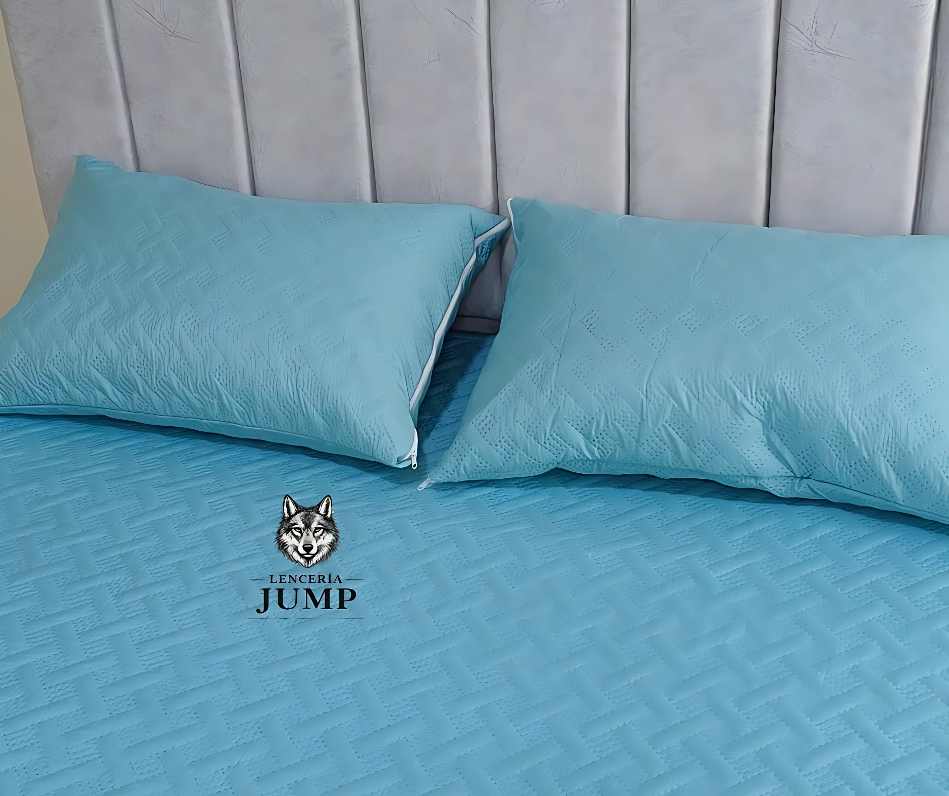 Set de dos almohadas de 70x50 cm en color azul claro, con funda termosellada y relleno de algodón siliconado, sobre cama con cabecero acolchado.