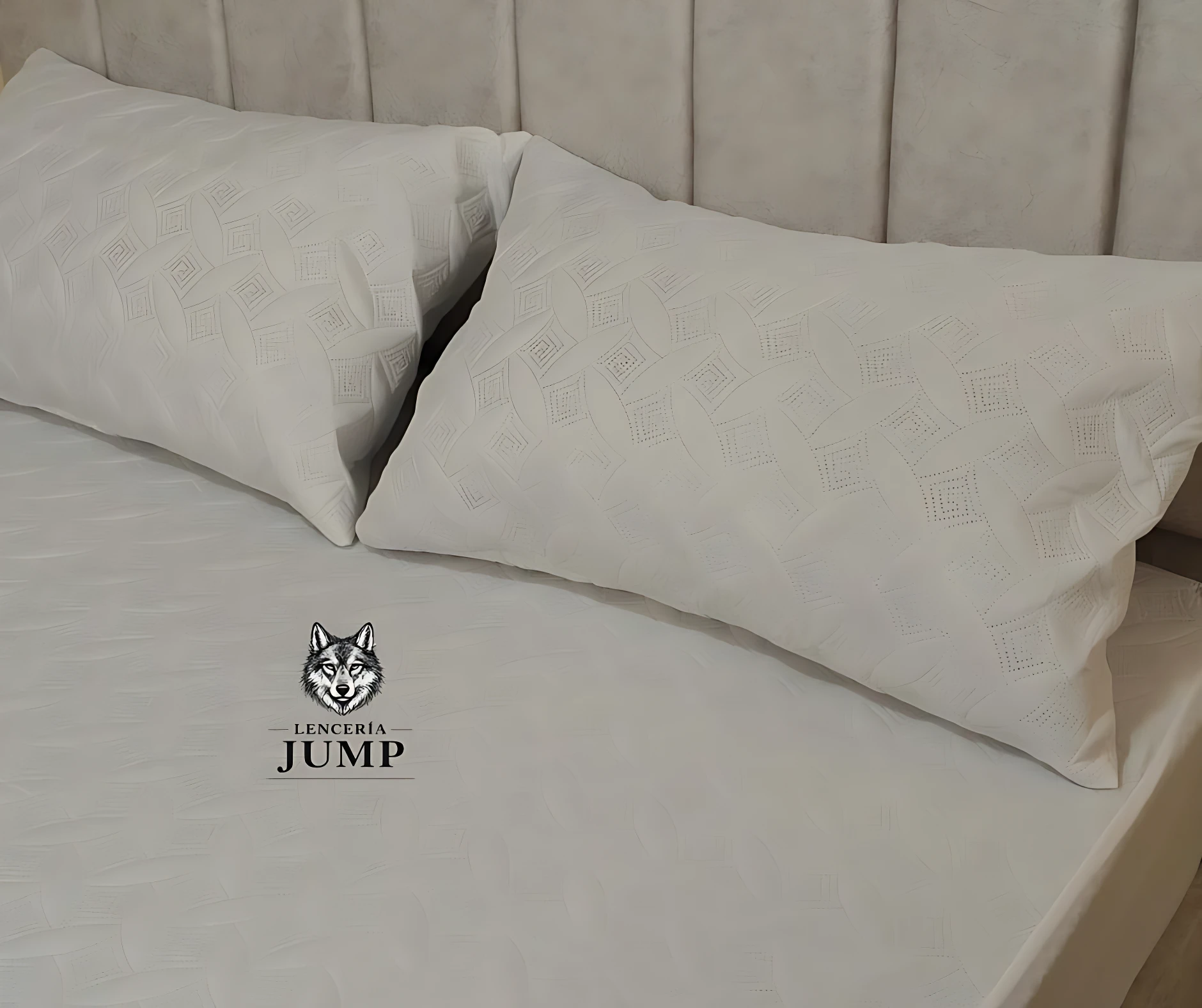 Dos almohadas blancas con textura geométrica, relleno de algodón siliconado, sobre cama con cabecero acolchado.