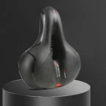 Asiento ergonómico negro con relieve central y textura perforada, diseñado para bicicletas de ruta; reduce presión en nalgas y mejora circulación.