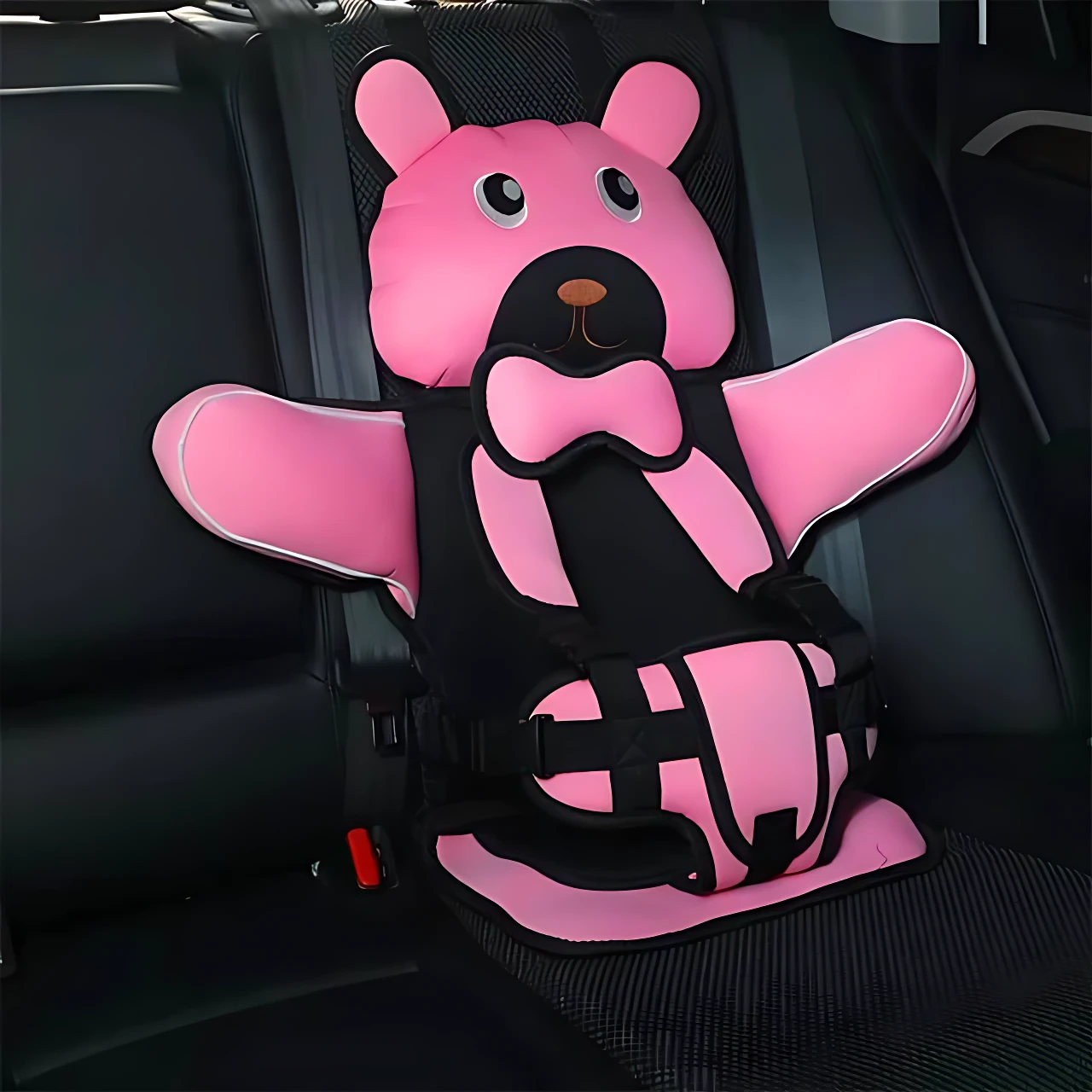 Asiento seguridad portátil para niños en color rosa con diseño de oso, instalado en asiento trasero de vehículo. Incluye arnés de tres puntos y almohadillas acolchadas.