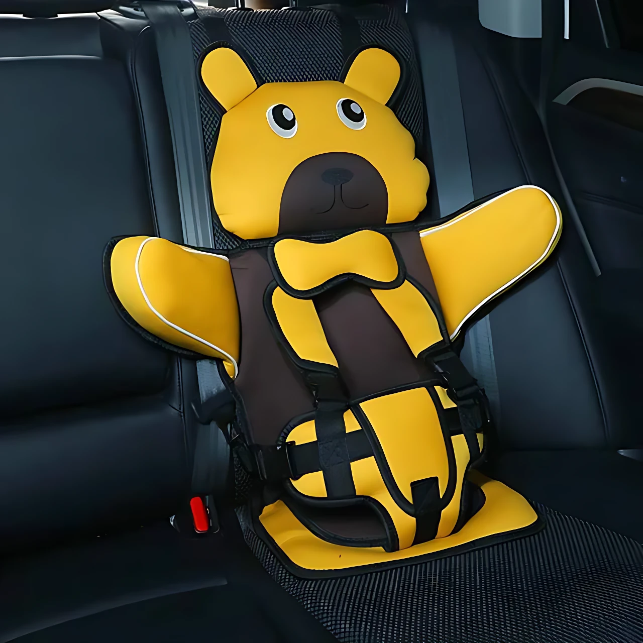 Asiento seguridad portátil para niños en forma de oso amarillo con detalles en marrón, instalado en asiento trasero de auto.