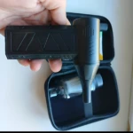 Aspiradora inalámbrica portátil negra con mango ergonómico, mostrada en mano junto a su estuche de transporte abierto que contiene accesorios internos.