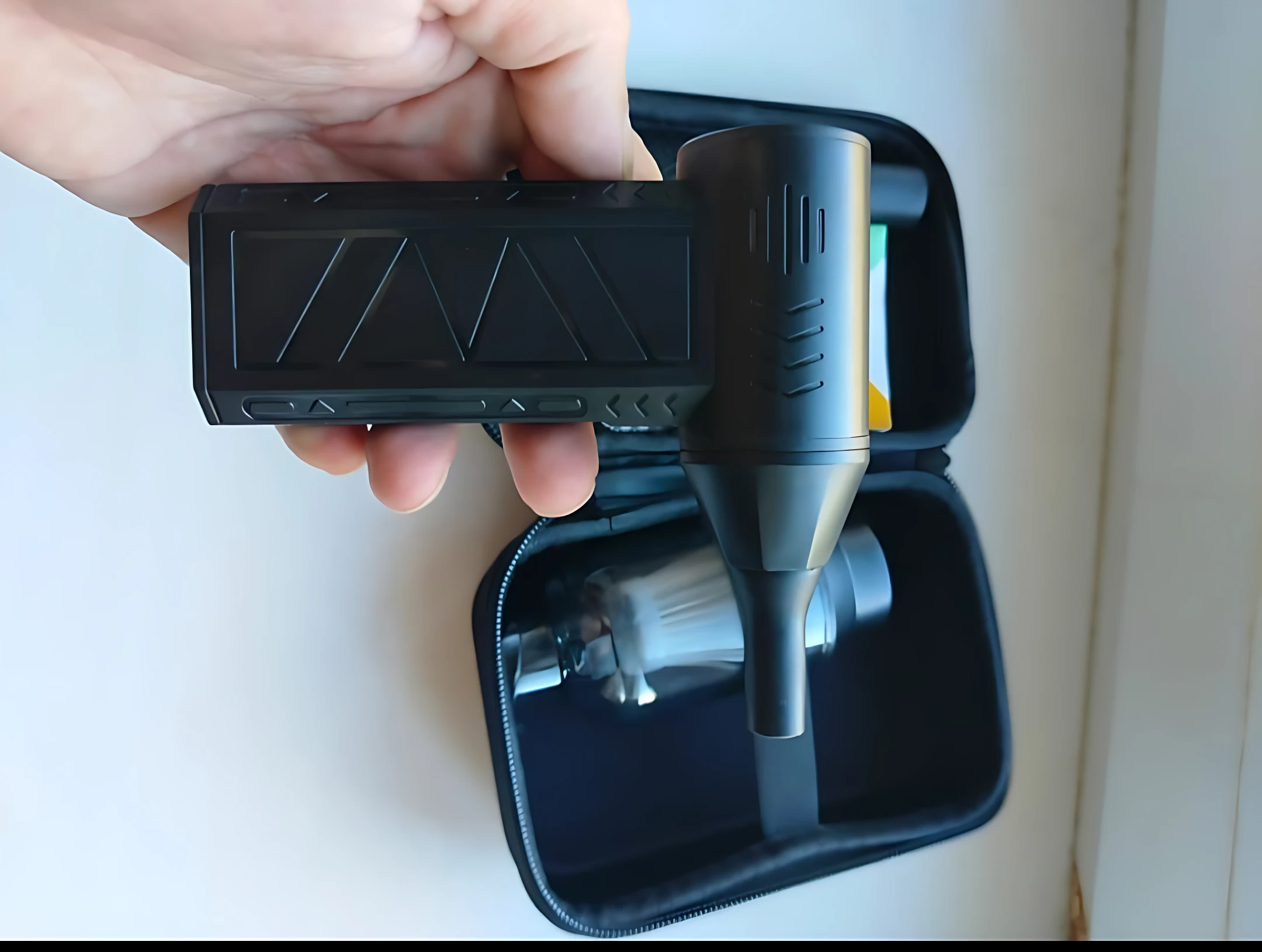 Aspiradora inalámbrica portátil negra con mango ergonómico, mostrada en mano junto a su estuche de transporte abierto que contiene accesorios internos.