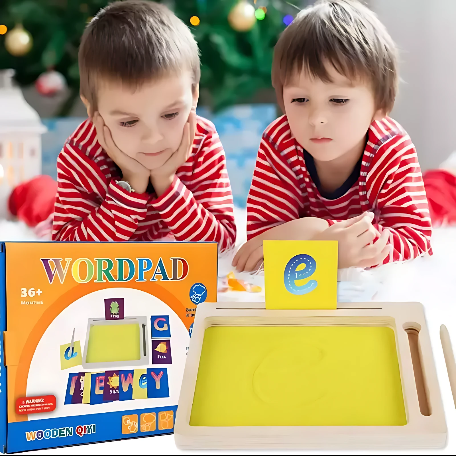Dos niños en pijama rojo y blanco observan una bandeja de arena magnética de madera con letras amarillas, junto a su caja que muestra el juego Wordpad.
