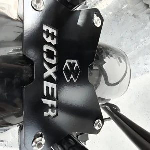 Placa de soporte negra con tornillos, marca Boxer y logotipo visible, instalada en estructura metálica de motocicleta.