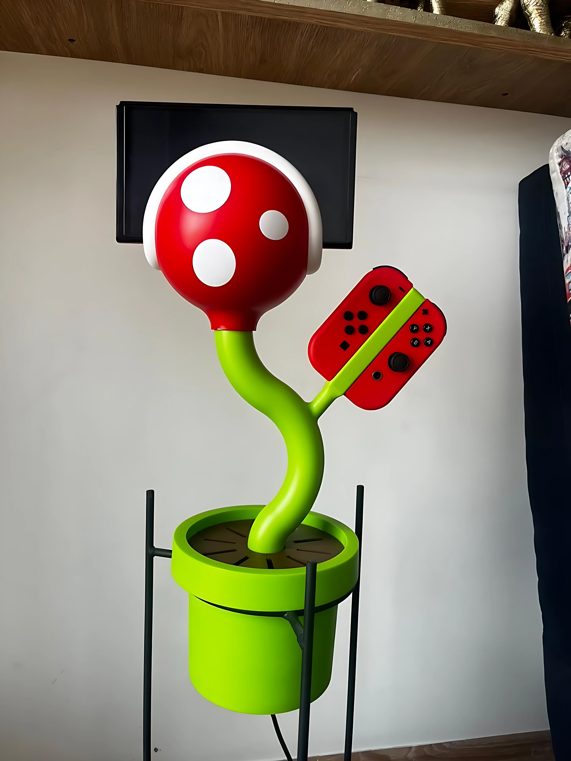 Soporte para consola y cartuchos con diseño de planta Piña Carnívora de Mario, en rojo, blanco y verde, sobre base de maceta.