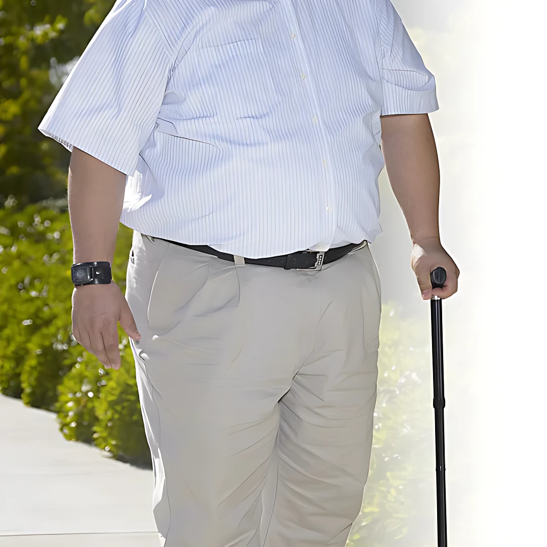 Hombre usando bastón plegable de aluminio negro con mango ergonómico, caminando al aire libre con camisa blanca y pantalón beige.