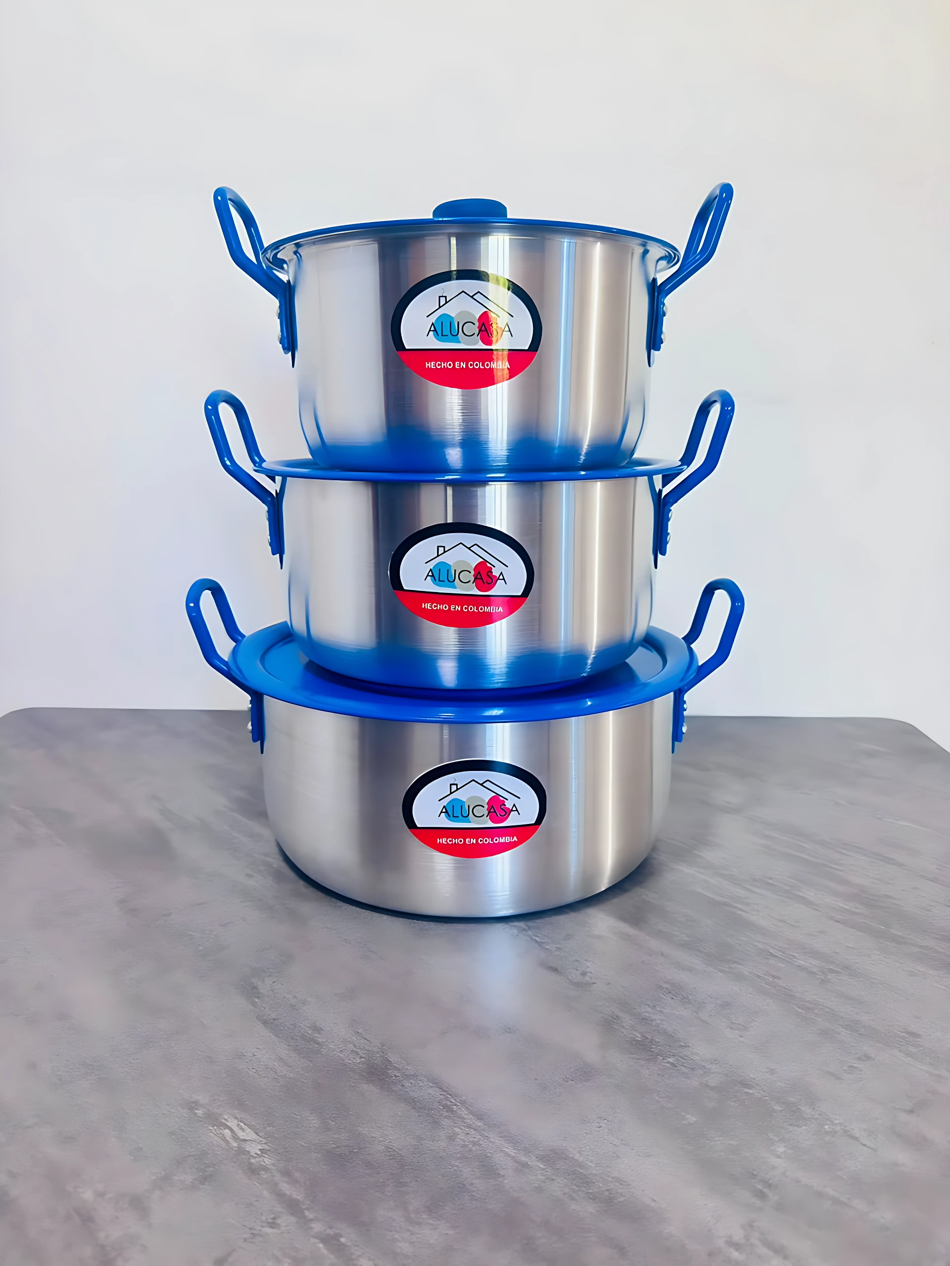 Tres ollas de acero inoxidable con asas azules apiladas, mostrando etiquetas con logo de marca.