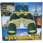 Binoculares de color verde y beige con lentes amarillos, sobre fondo con imágenes de paisajes y monumentos. Caja con texto multilingüe y frase promocional en español.