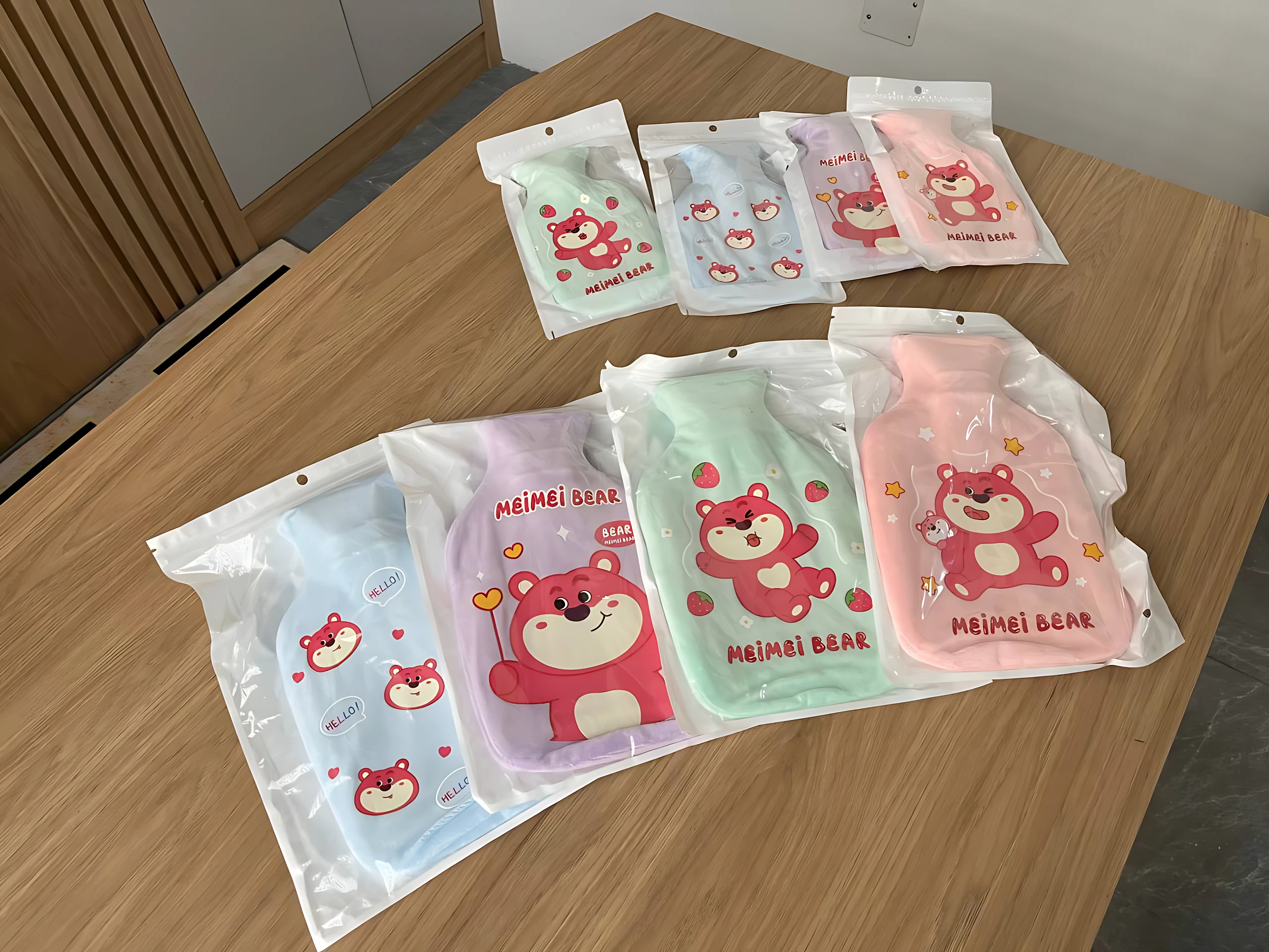 Set de dos bolsas de agua caliente con diseño de oso Meimei Bear en colores pastel, dispuestas sobre superficie de madera.