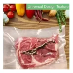 Bolsa de empaque al vacío transparente con carne cruda y hierbas, sobre superficie de madera con vegetales frescos al fondo.