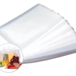 Bolsa de empaque al vacío transparente, apilada en diagonal sobre fondo blanco, con inserto circular mostrando alimentos frescos como queso, uvas y vegetales dentro de la bolsa sellada.