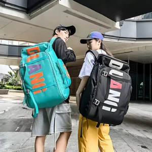 Dos modelos usan mochilas grandes con diseño urbano; una en color turquesa con letras naranjas y moradas, la otra negra con letras blancas y rojas, ambas con múltiples compartimentos visibles.