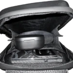 Bolso cruzado hombre cuero sintético negro abierto mostrando estuche de audífonos y teléfono móvil dentro de compartimento acolchado.