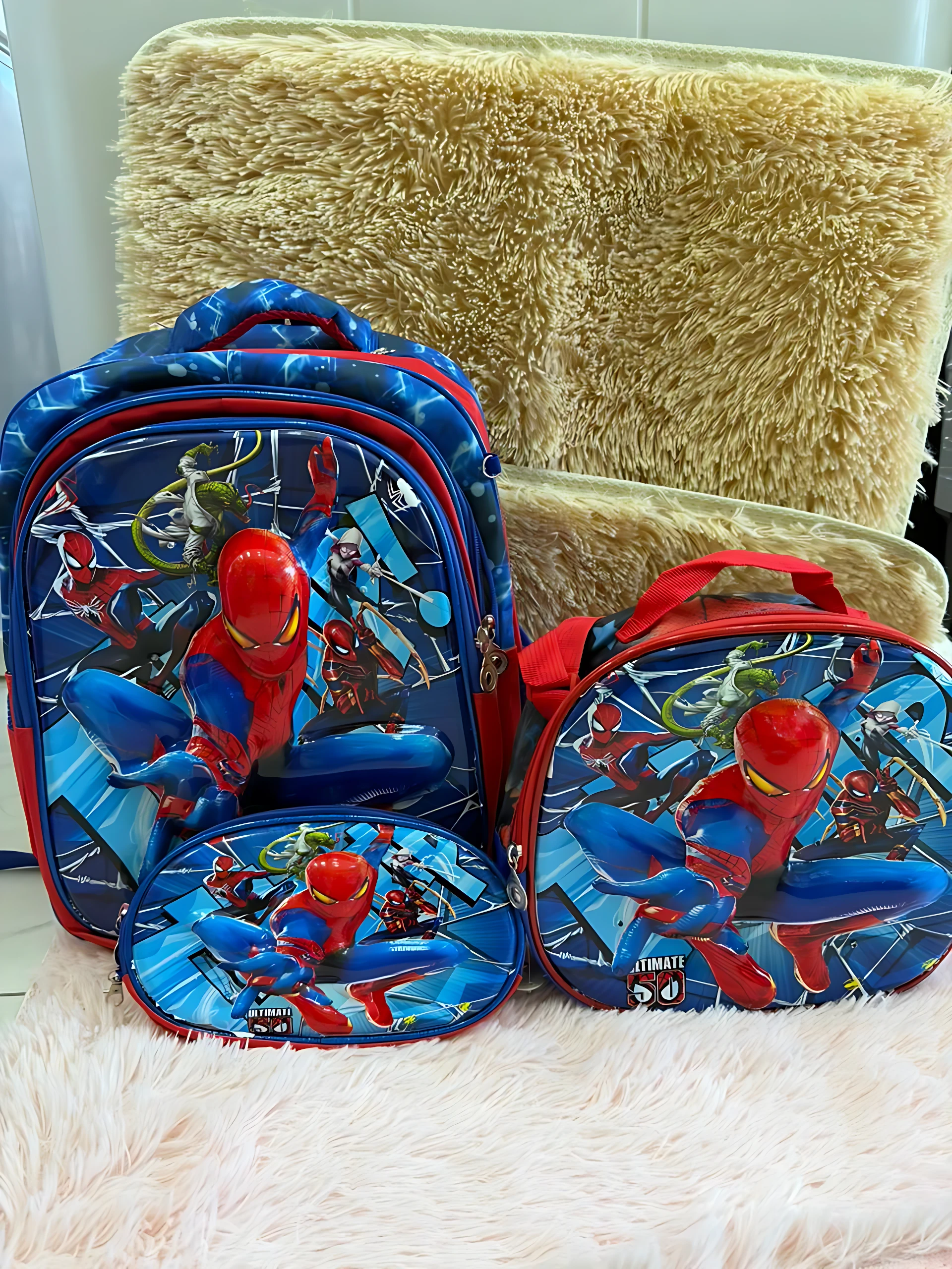 Mochila escolar Spiderman en azul y rojo con lonchera y cartuchera, sobre superficie blanca y fondo beige.