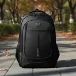 Mochila urbana Oxford negra de 45 litros, con compartimento para laptop de 17 pulgadas, visible en primer plano sobre camino adoquinado con hojas caídas.