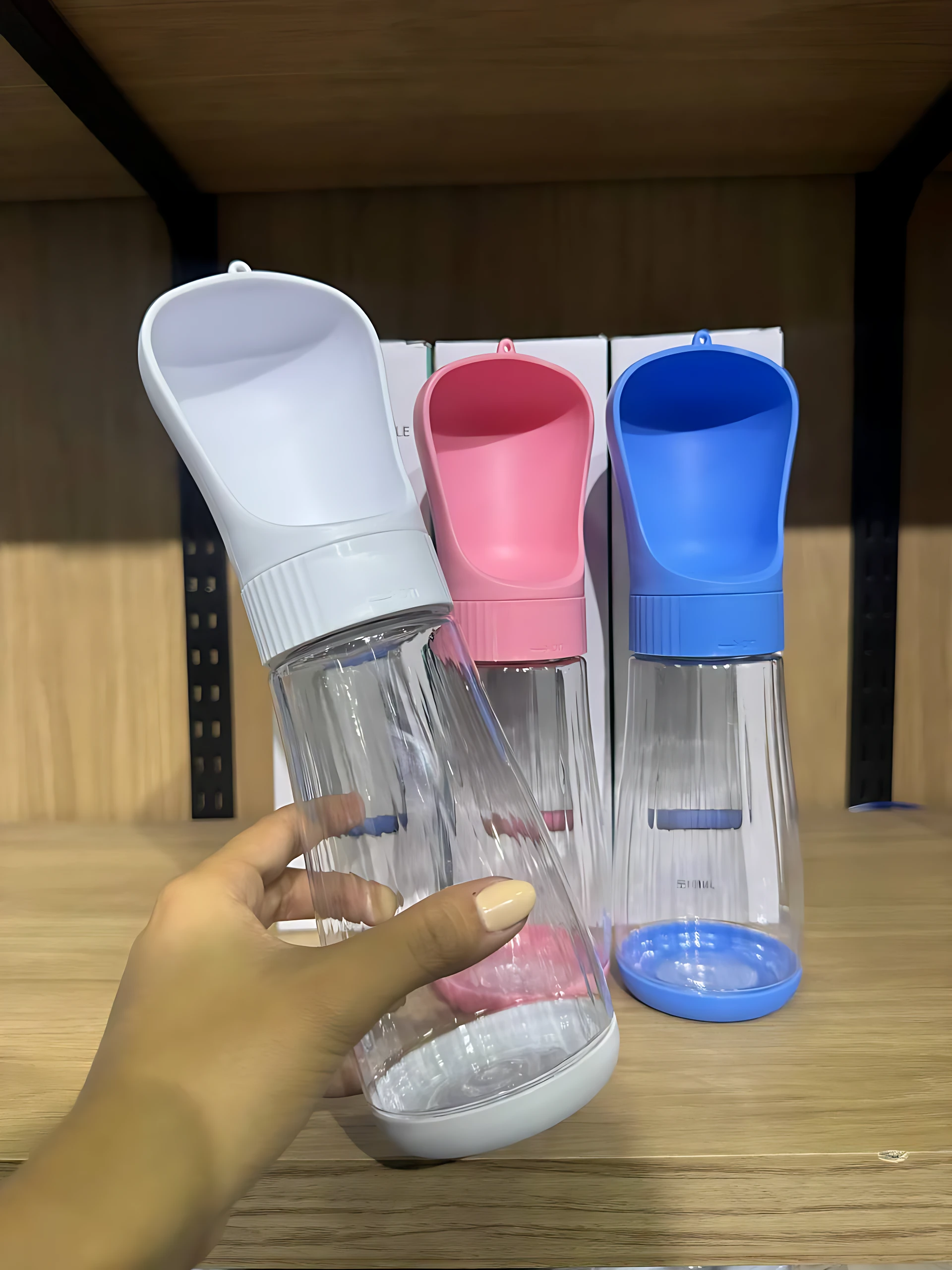 Botella bebedero portátil con depósito integrado, en tres colores: blanco, rosa y azul. Diseño ergonómico para hidratación de mascotas en viajes.