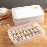 Caja de almacenamiento para congelador con tapa blanca y cierre verde, mostrando su interior con galletas dispuestas en filas sobre superficie de madera.