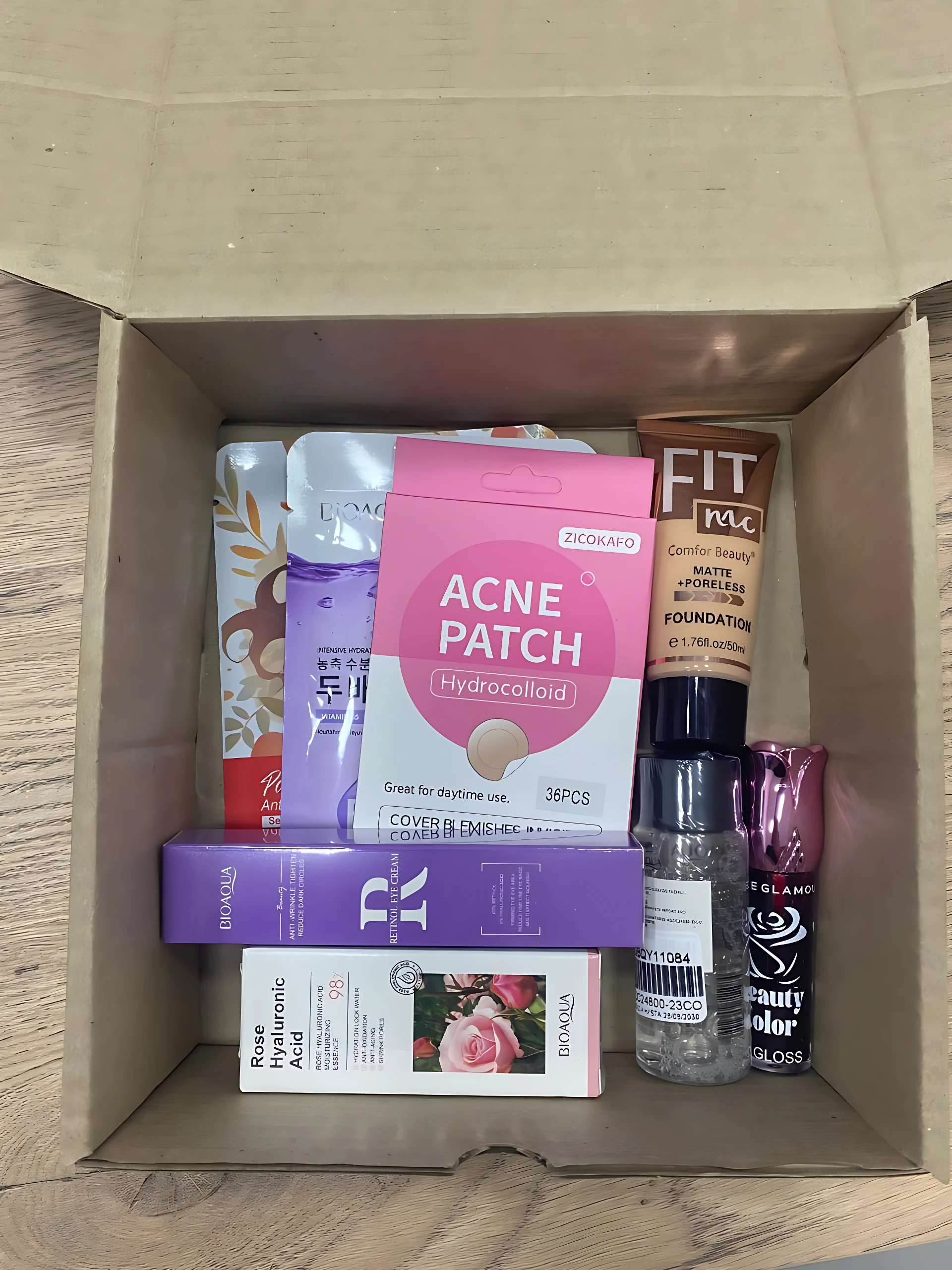 Caja abierta con productos de cuidado facial y maquillaje: parches de acné, base, labial, esmalte y otros accesorios dispuestos en interior.