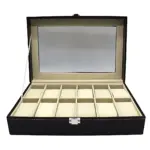 Caja organizadora de relojes negra con cristal superior, interior beige con 12 compartimentos individuales y cierre metálico frontal.