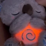 Peluche koala blanco de peluche con luz naranja en el pecho y espiral azul, cerrado los ojos, ideal para dormir.