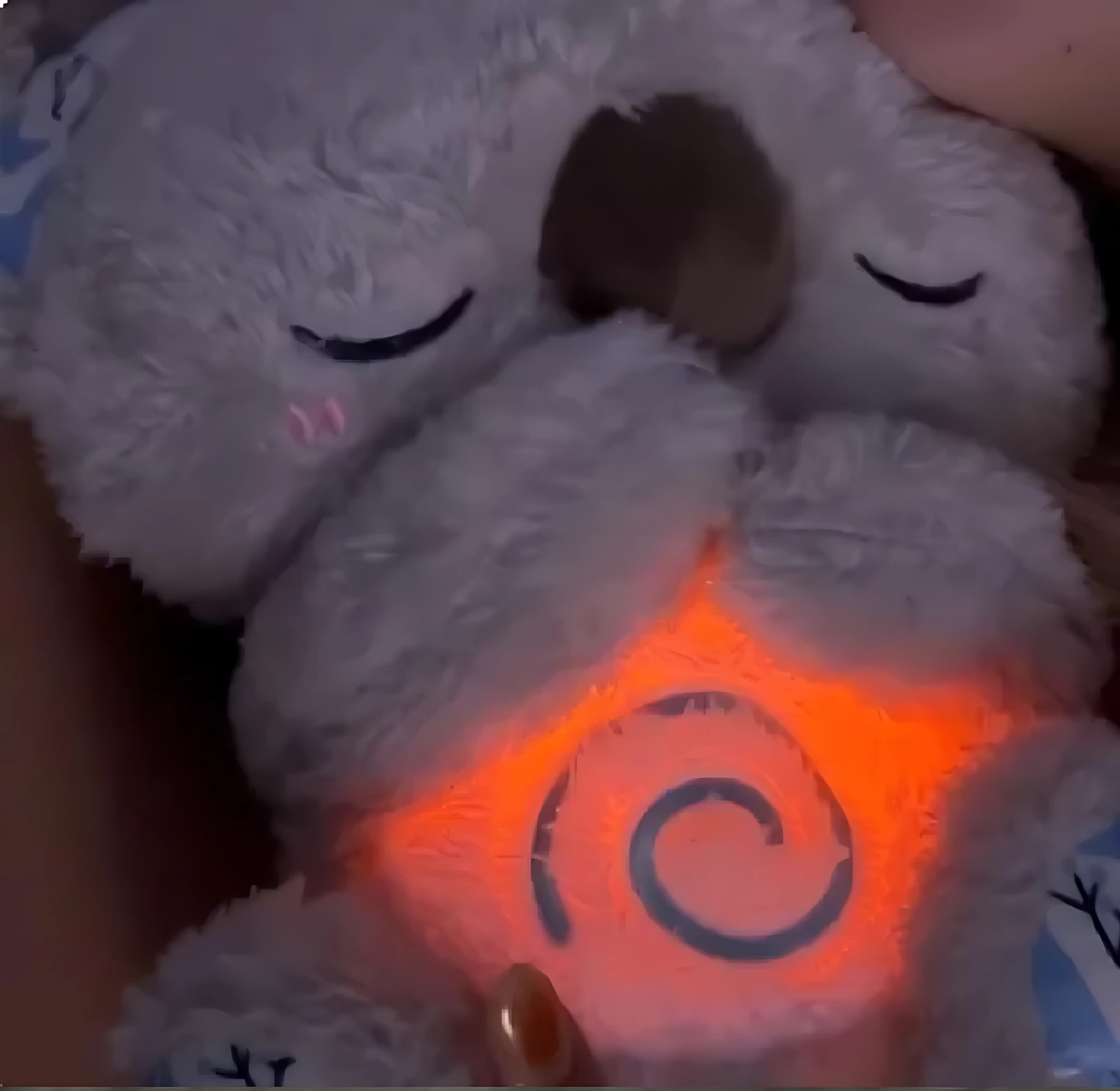 Peluche koala blanco de peluche con luz naranja en el pecho y espiral azul, cerrado los ojos, ideal para dormir.