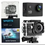 Cámara deportiva negra con carcasa transparente, caja de presentación y accesorios de montaje. Muestra detalles como lente frontal, botón de encendido y etiqueta HD 1080P. Incluye caja con de surfista y texto "Action Camera".