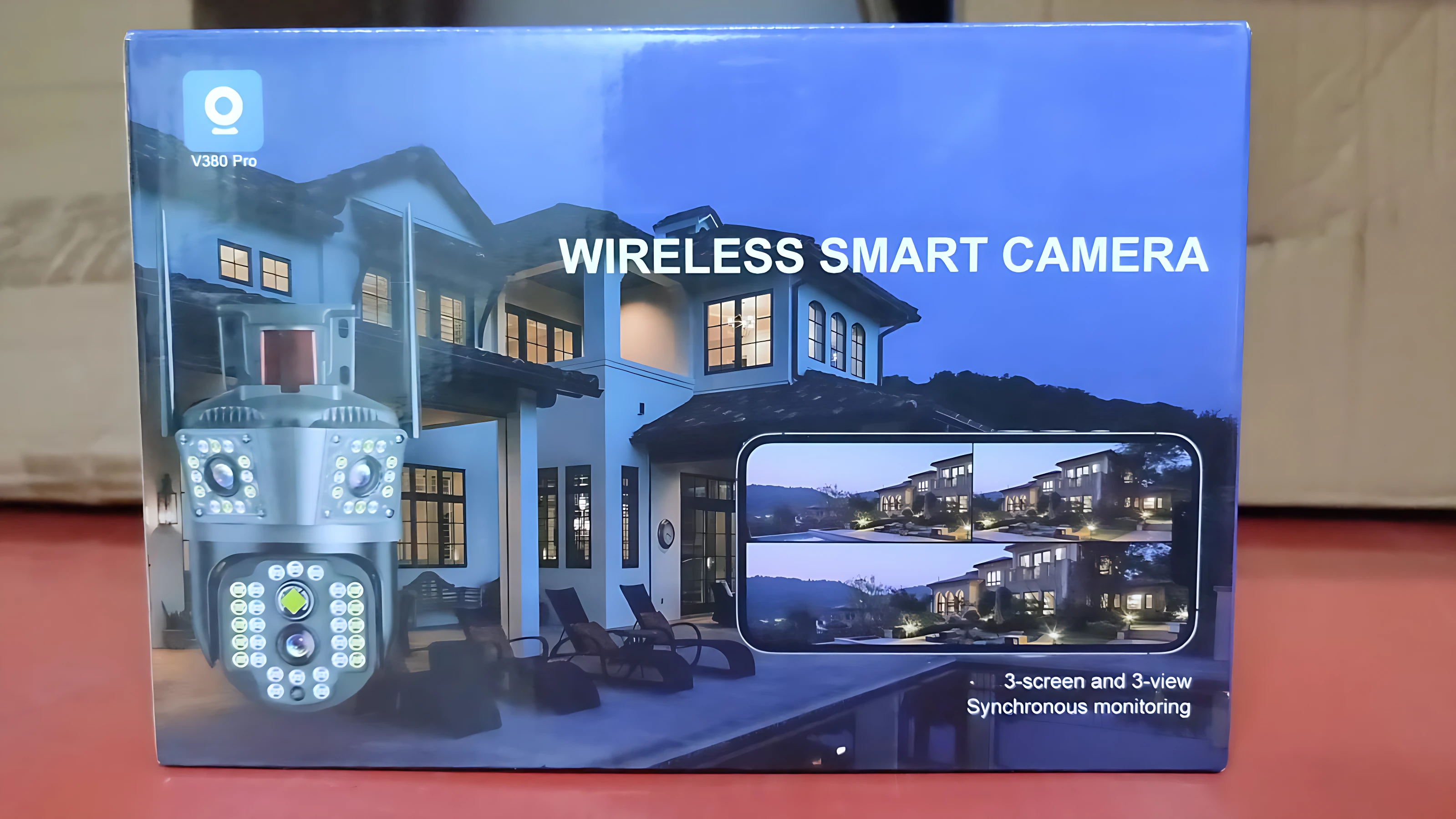 Cámara exterior inalámbrica con tres lentes y alarma 4G, mostrada en su caja azul con de casa y pantalla de monitoreo.