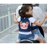 Arnés de seguridad para niños en azul marino con diseño de oso, usado por niña montada en moto eléctrica, con cinturón ajustable y respaldo acolchado.