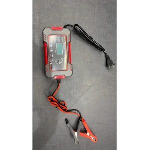 Cargador inteligente de batería 12V con pantalla digital, cables rojo y negro y pinzas de conexión, sobre superficie gris texturizada.