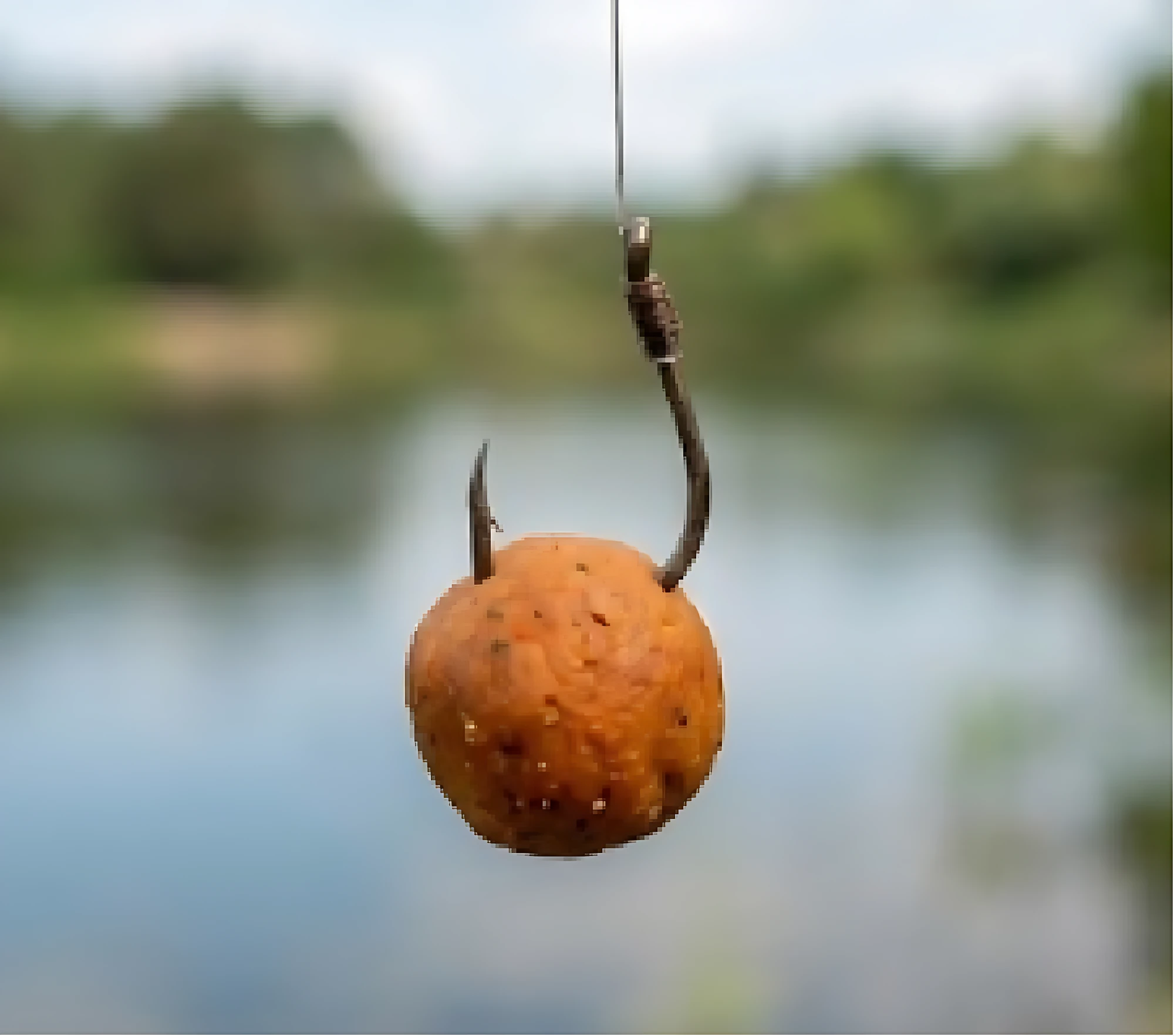 Masa de pesca natural chontaduro en forma esférica, color naranja con textura granulada, montada sobre anzuelo doble, suspendida frente a fondo de río borroso.