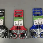 Tres carretas plegables de aluminio en negro, rojo y azul, con capacidad para 75 kg, mostradas en vista frontal sobre superficie gris.