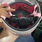 Casco juvenil Capibara KURSTUER color crema con visor extendido, interior rojo y correa rosa, mostrando sistema de ajuste central y detalles de protección facial.