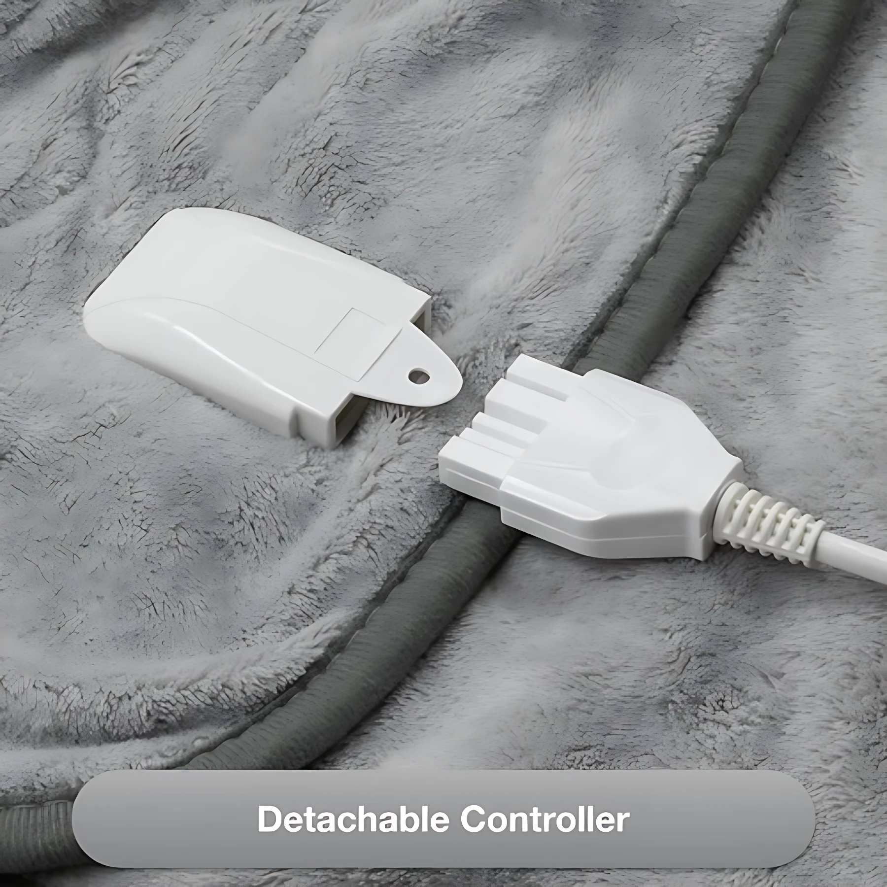 Control desmontable blanco de cobija eléctrica sobre tela de felpa gris, con cable conectado y botón visible.