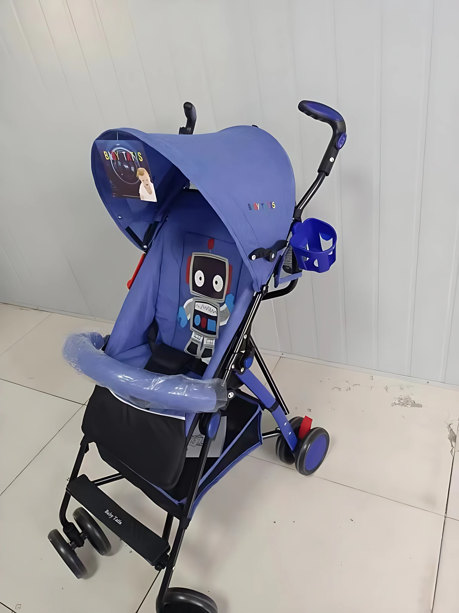 Coche paseador tipo sombrilla en color azul con capota protectora, asiento acolchado y detalles gráficos de robot. Incluye reposapiés ajustable, manillar ergonómico y ruedas pequeñas para desplazamiento suave. Ideal para uso diario y viajes cortos.