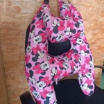 Cojín de viaje en forma de H con estampado de Minnie Mouse en rosa y negro, colgado sobre respaldo de silla.
