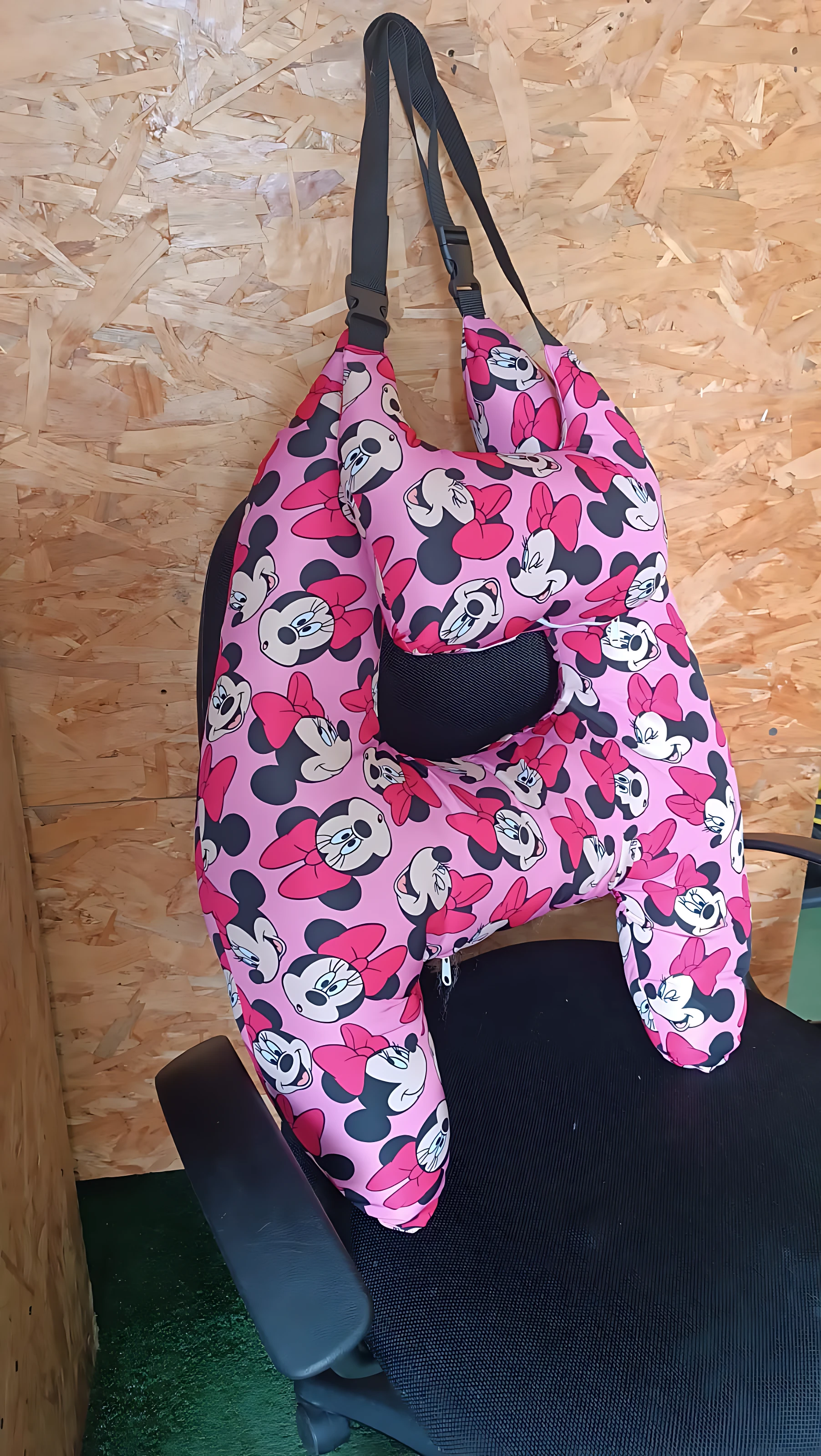 Cojín de viaje en forma de H con estampado de Minnie Mouse en rosa y negro, colgado sobre respaldo de silla.
