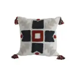 Cojín decorativo blanco con bordado en relieve geométrico en negro y rojo, detalles en borlas multicolores en las esquinas.