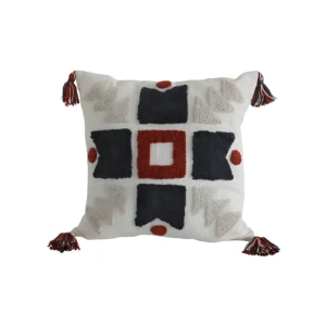 Cojín decorativo blanco con bordado en relieve geométrico en negro y rojo, detalles en borlas multicolores en las esquinas.