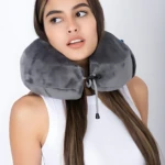 Cojín cervical gris con cordón ajustable, usado por mujer joven en pose de viaje.