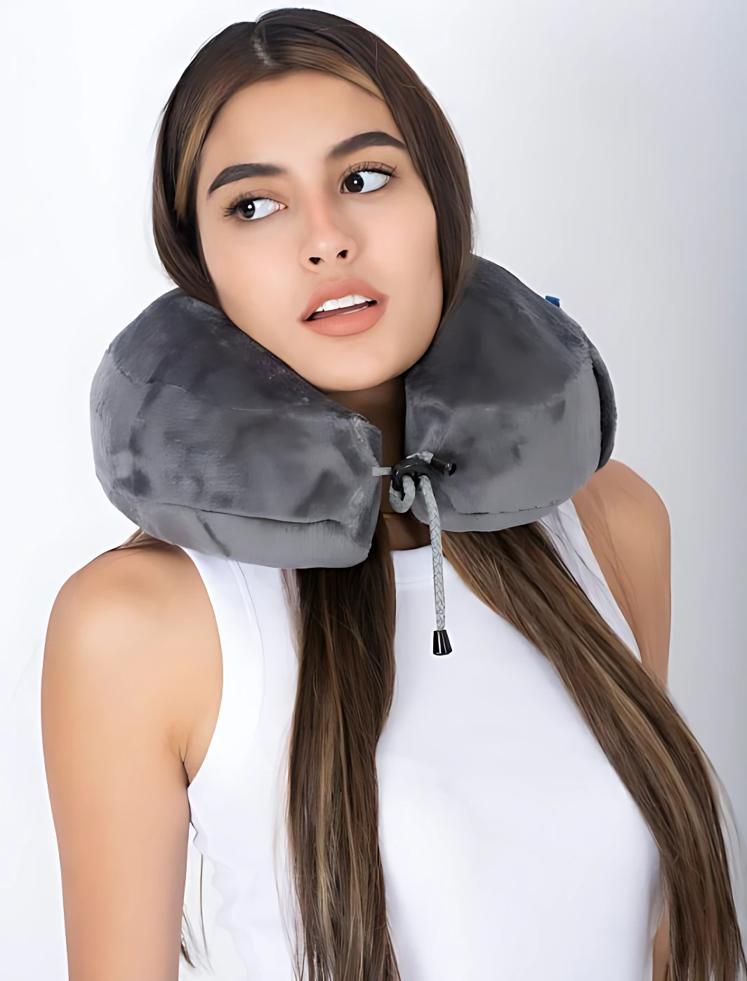 Cojín cervical gris con cordón ajustable, usado por mujer joven en pose de viaje.