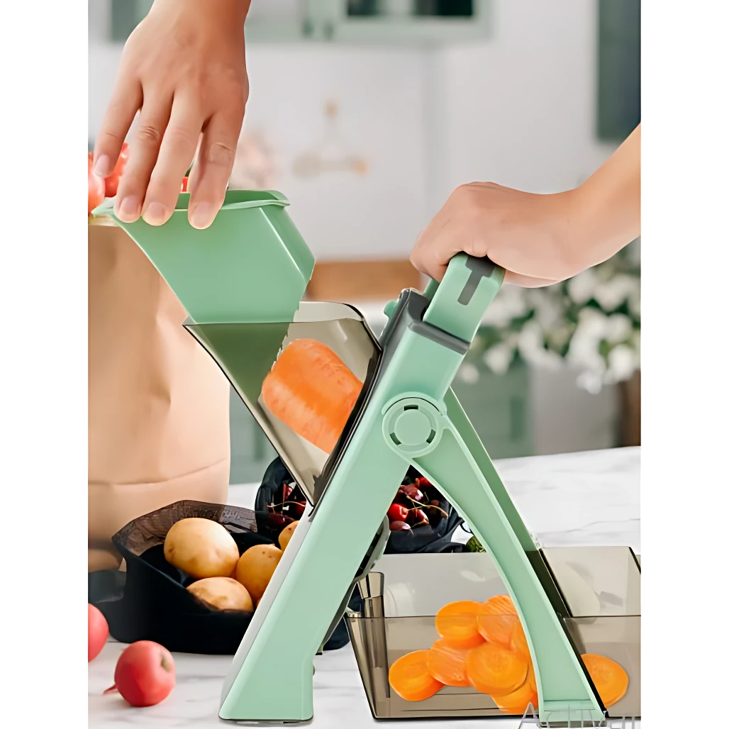 Cortador mandolina verde menta en uso, con mango de seguridad y bandeja colectora transparente; manos ajustan vegetales para corte uniforme.