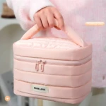 Cosmetiquera compacta en color rosa pastel, con cremallera frontal y asa ergonómica. Presenta textura acolchada y etiqueta visible que dice "BEEN LOVE". Ideal para organizar maquillaje y accesorios de forma práctica y estética.