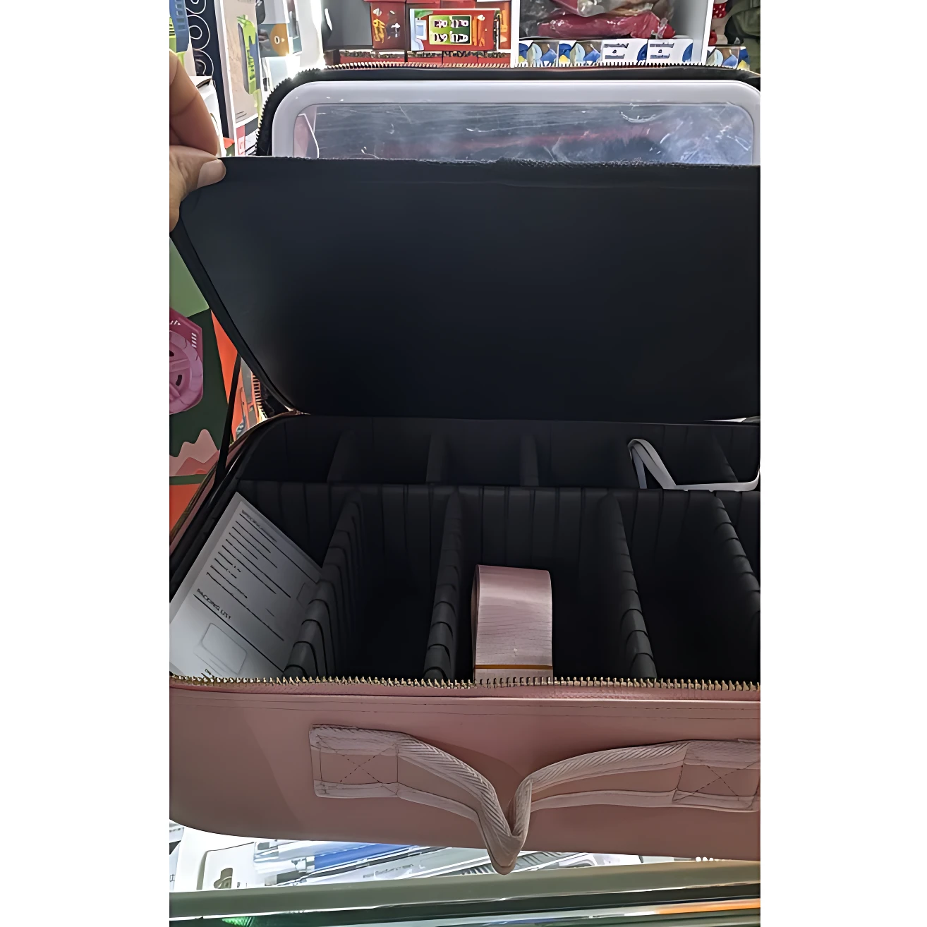 Tocador portátil rosa con compartimentos organizadores negros, tapa transparente y asa de tela, abierto para mostrar interior.