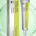 Set de dos unidades de crema facial Retinol en tubo y caja, con etiqueta amarilla y texto negro sobre fondo blanco, sobre superficie verde translúcida.
